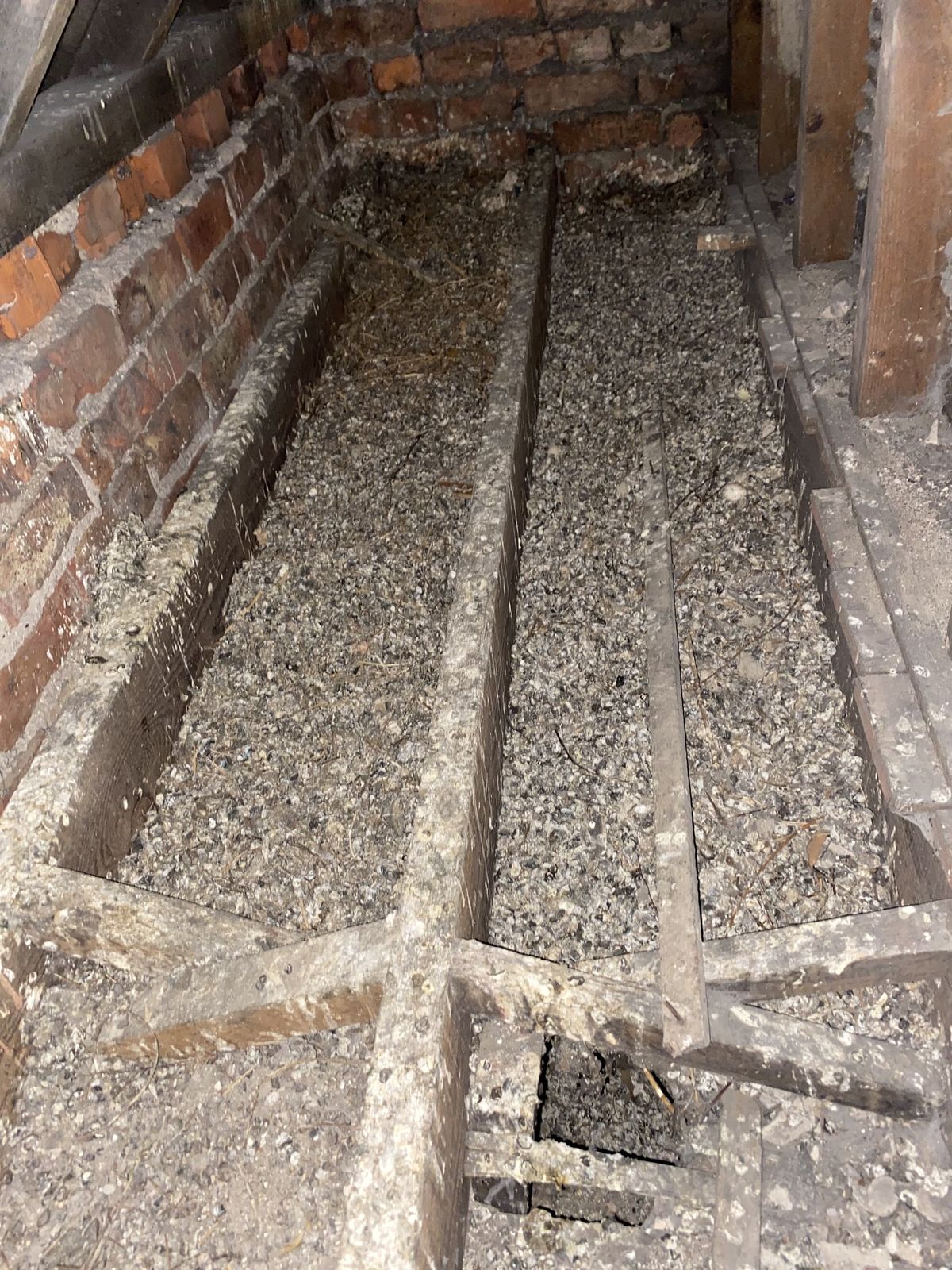 An opened floor void between brick walls, with joists and debris, on a Pestguard job