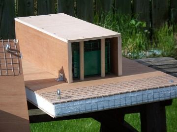 A wooden box trap on a mesh-topped platform outdoors