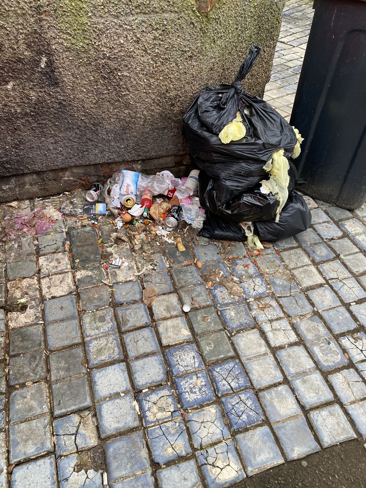 A torn bin bag with rubbish scattered on block paving